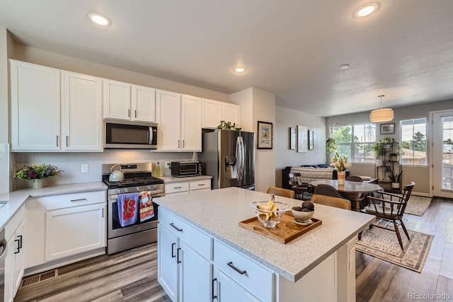 kitchen featuring pendant lighting, stainless steel appliances, a center island, light hardwood / wood-style floors, and white cabinets