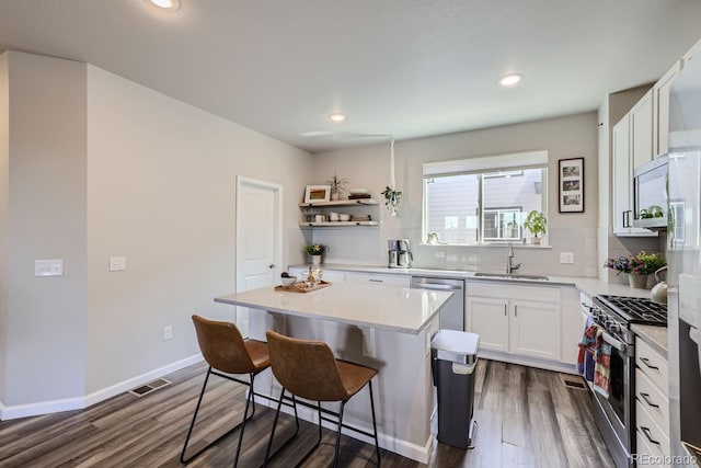 kitchen with appliances with stainless steel finishes, white cabinetry, sink, a center island, and dark wood-type flooring