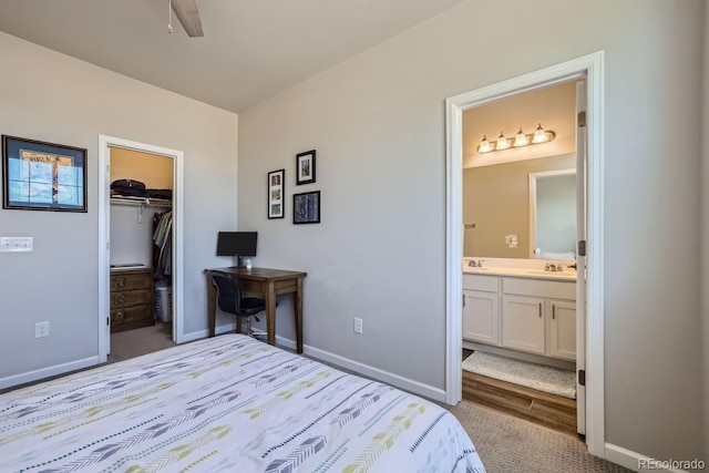 carpeted bedroom with ceiling fan, a walk in closet, connected bathroom, and sink