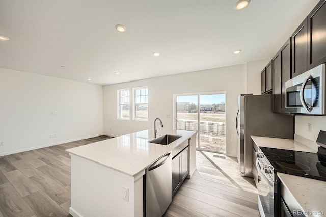 kitchen with recessed lighting, stainless steel appliances, a sink, light wood-style floors, and a center island with sink