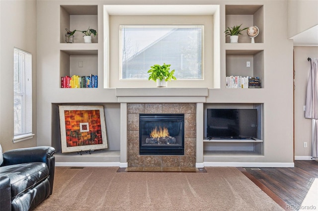 living room featuring baseboards, wood finished floors, a tile fireplace, and built in features