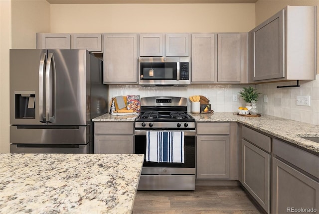 kitchen featuring decorative backsplash, gray cabinetry, dark hardwood / wood-style flooring, light stone counters, and stainless steel appliances