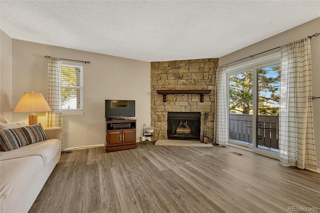 living room featuring wood-type flooring, a stone fireplace, and a textured ceiling