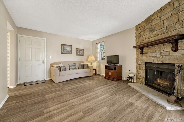 living room featuring wood-type flooring, a stone fireplace, and a textured ceiling