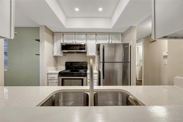 kitchen with a raised ceiling, white cabinetry, and appliances with stainless steel finishes