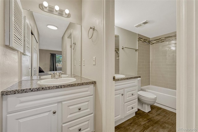 full bathroom featuring vanity, hardwood / wood-style flooring, tiled shower / bath combo, and toilet