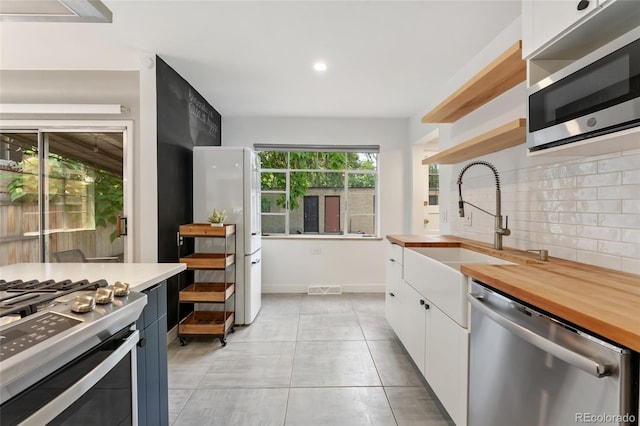1579 Fairfax St, Denver, CO 80220 - kitchen with appliances with stainless steel finishes, open shelves, white cabinets, backsplash, and butcher block countertops