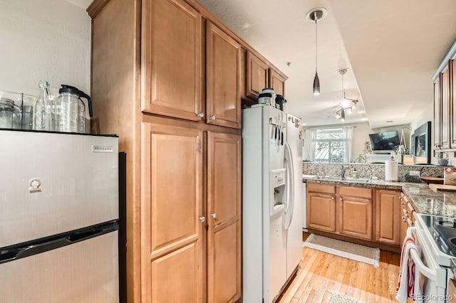 3030 Wyandot St Unit 7, Denver, CO 80211 - kitchen with white appliances, light wood-style floors, brown cabinets, hanging light fixtures, and dark stone countertops