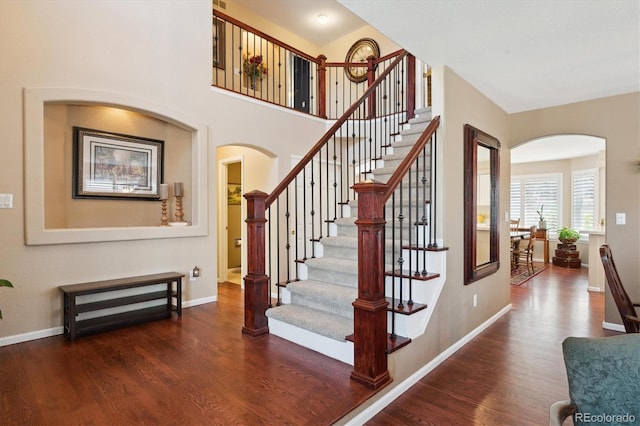 stairs featuring baseboards, arched walkways, and wood finished floors