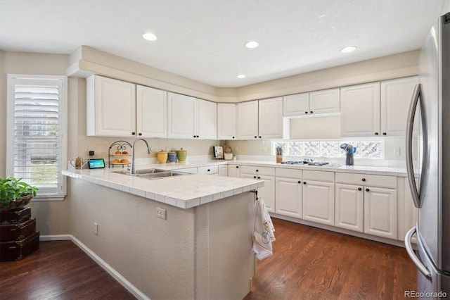 kitchen featuring white cabinets, a sink, freestanding refrigerator, a peninsula, and tile countertops