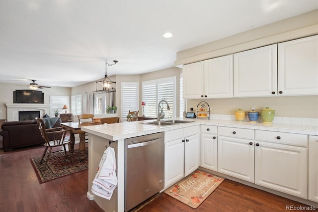 kitchen with tile countertops, stainless steel dishwasher, a sink, a peninsula, and dark wood-style floors