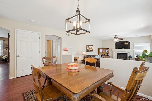 dining room featuring visible vents, a fireplace, arched walkways, dark wood finished floors, and ceiling fan with notable chandelier