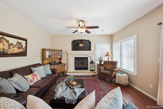 living room featuring baseboards, ceiling fan, a tile fireplace, and wood finished floors