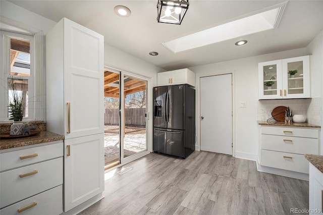 kitchen featuring tasteful backsplash, light wood-style floors, a skylight, white cabinets, and black refrigerator with ice dispenser