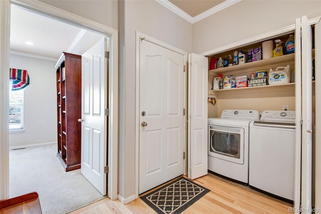 clothes washing area with laundry area, ornamental molding, washer and clothes dryer, and light wood finished floors