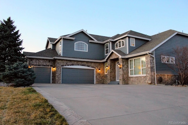 view of front of property with stone siding, driveway, a shingled roof, and an attached garage