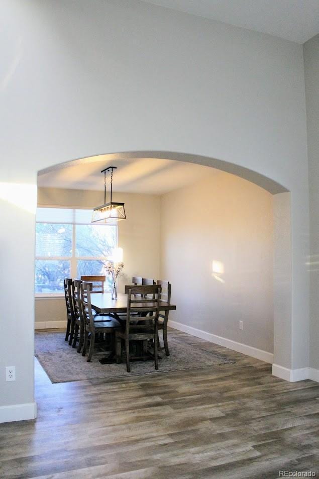 dining space with wood finished floors, arched walkways, and baseboards