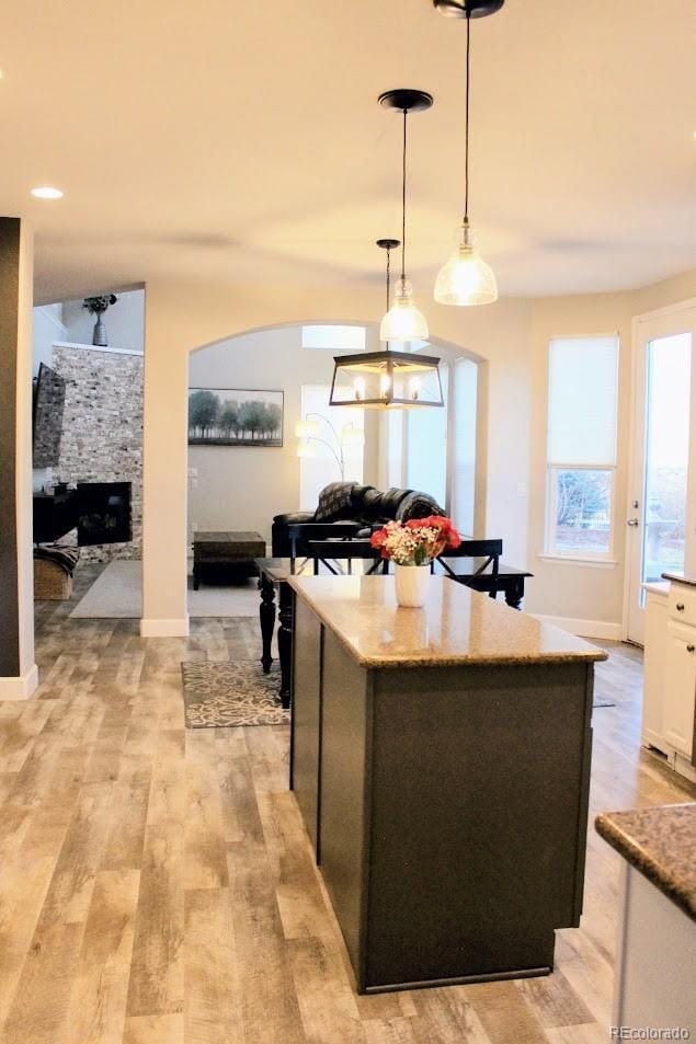 kitchen featuring light stone counters, a fireplace, light wood-style floors, pendant lighting, and white cabinetry