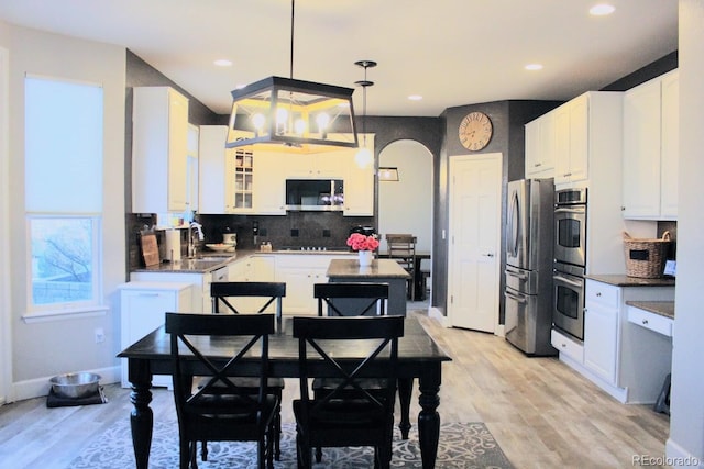 kitchen with arched walkways, a sink, stainless steel appliances, white cabinets, and light wood-style floors