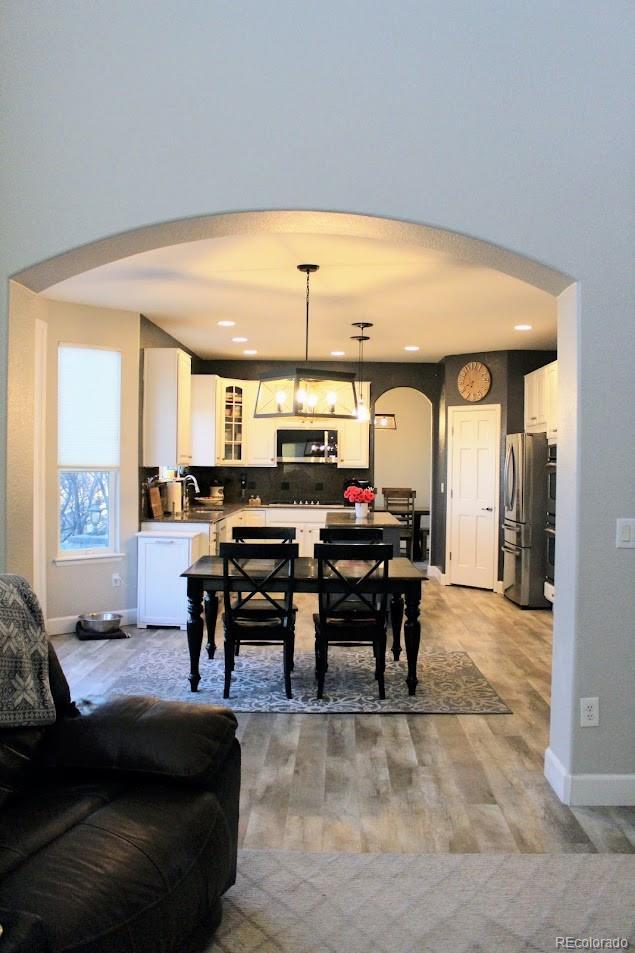 dining area with arched walkways, a chandelier, light wood-type flooring, and baseboards