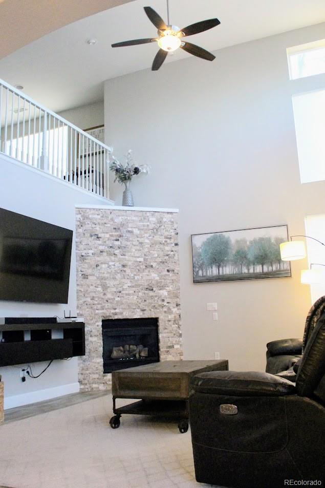 living room featuring a fireplace, a ceiling fan, and a towering ceiling