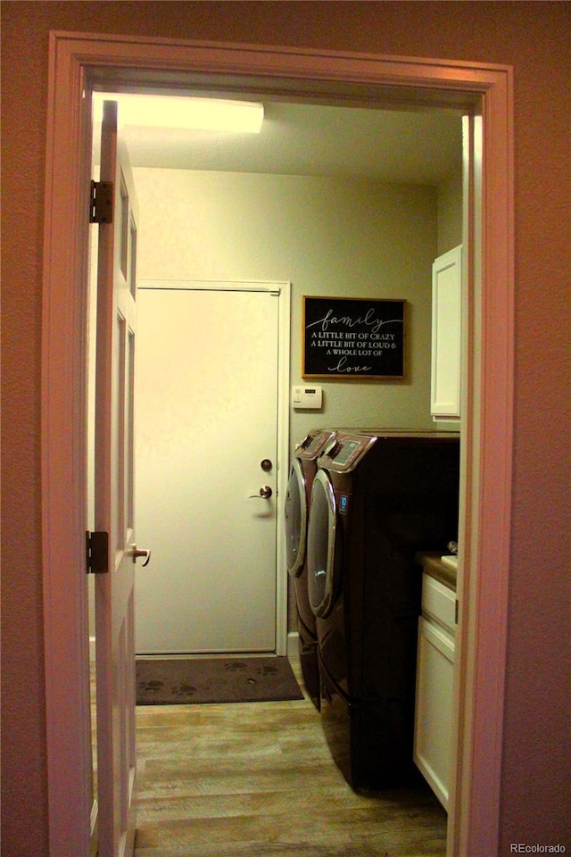 clothes washing area with washer and dryer, wood finished floors, and cabinet space