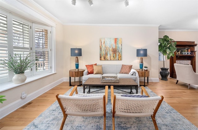 living area with healthy amount of natural light, baseboards, light wood-style floors, and crown molding