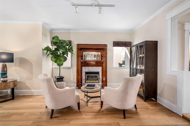 sitting room featuring light wood finished floors, baseboards, a glass covered fireplace, crown molding, and rail lighting