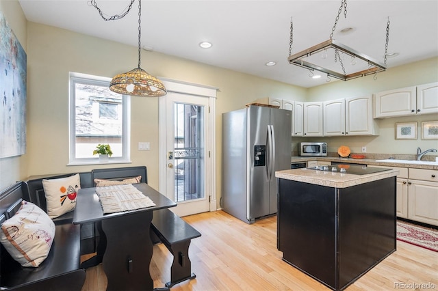 kitchen with stainless steel appliances, a sink, light countertops, pendant lighting, and light wood-type flooring