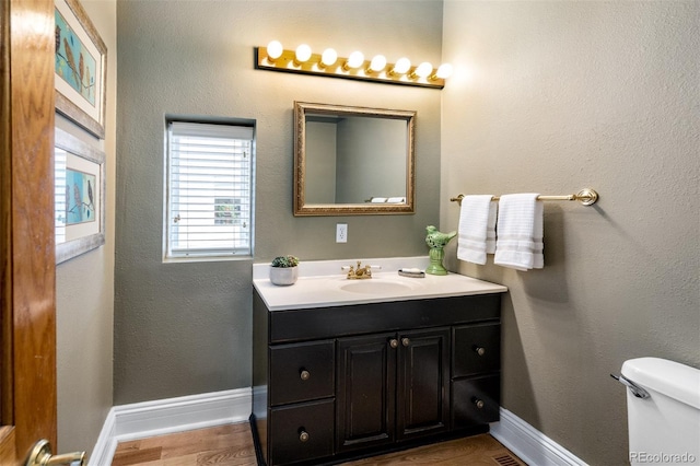 half bathroom with vanity, toilet, baseboards, and wood finished floors