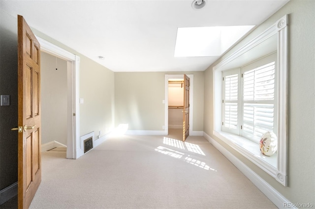 unfurnished bedroom with a skylight, light carpet, baseboards, and a spacious closet