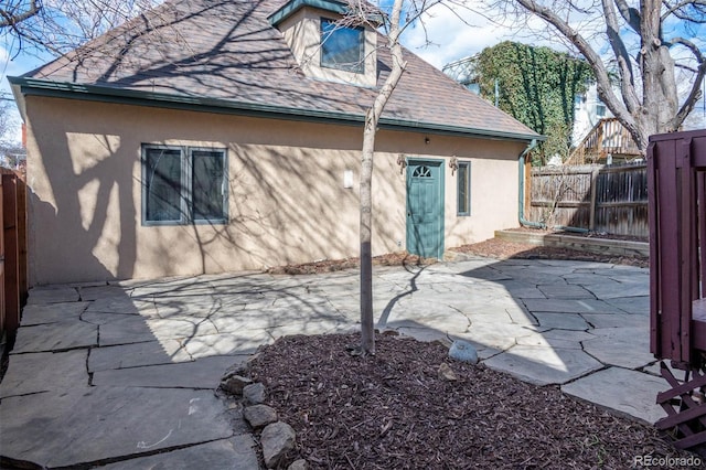 view of home's exterior with stucco siding, a patio area, a fenced backyard, and roof with shingles