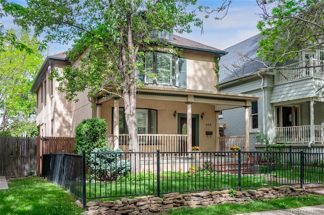 victorian house with covered porch, stucco siding, and a fenced front yard