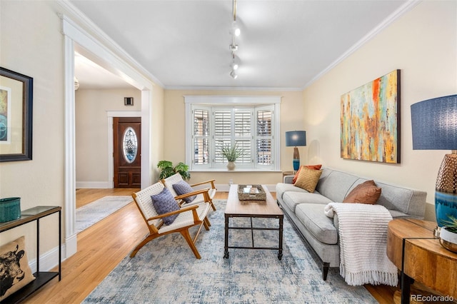 living area with wood finished floors, ornamental molding, baseboards, and rail lighting