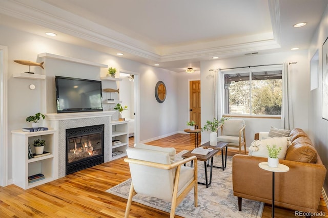 living room with a tiled fireplace, hardwood / wood-style flooring, and a tray ceiling