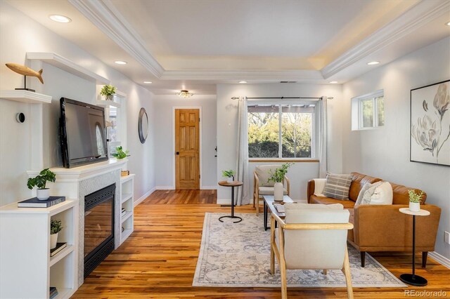 living room featuring crown molding, light hardwood / wood-style floors, and a tray ceiling