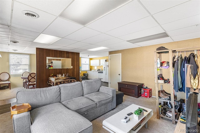 living room featuring light colored carpet, a drop ceiling, and wooden walls