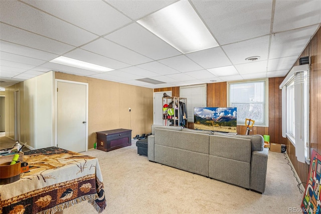 living room with light colored carpet, a paneled ceiling, and wooden walls