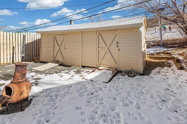 snow covered structure with an outbuilding, fence, and a shed