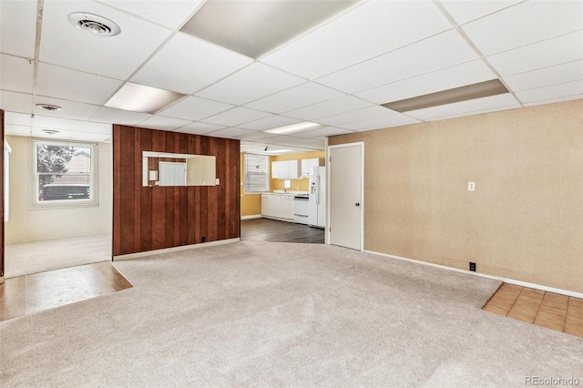 carpeted empty room featuring a paneled ceiling, wood walls, and visible vents