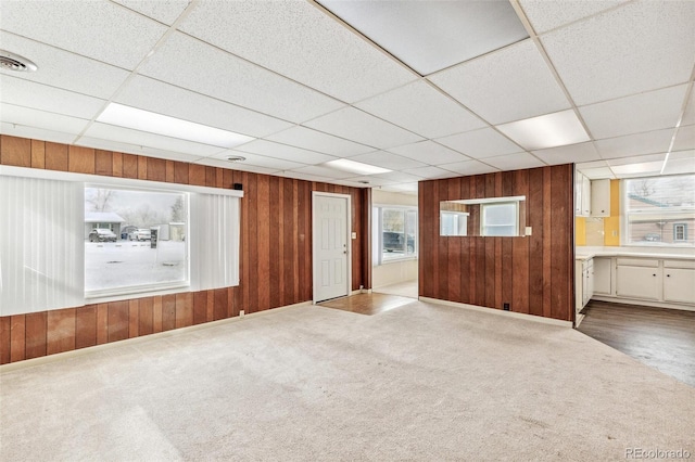 empty room with a paneled ceiling, wooden walls, visible vents, and light colored carpet