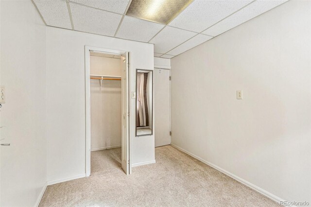 unfurnished bedroom featuring baseboards, light colored carpet, a spacious closet, a paneled ceiling, and a closet