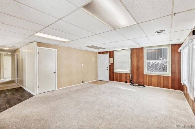 carpeted spare room with a paneled ceiling, wood walls, and visible vents