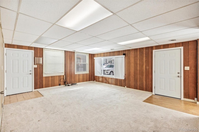 interior space with a paneled ceiling, wooden walls, and light colored carpet