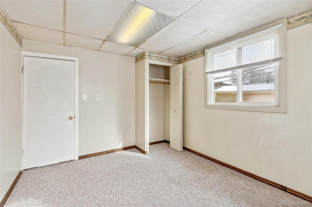 unfurnished bedroom featuring carpet, a closet, a drop ceiling, and baseboards