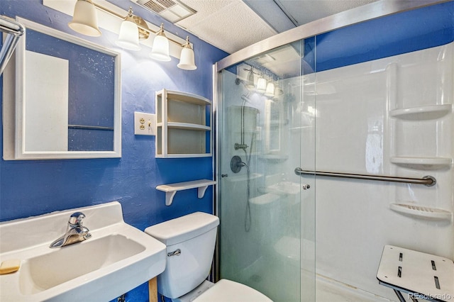 bathroom featuring visible vents, a textured wall, toilet, a shower stall, and a sink