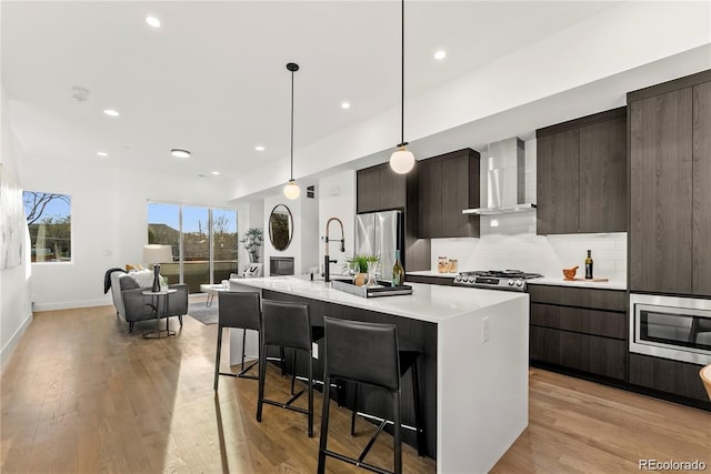 kitchen with appliances with stainless steel finishes, light countertops, wall chimney range hood, and modern cabinets