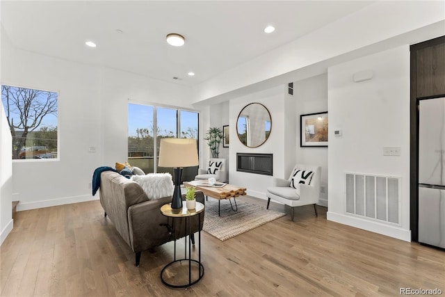 living room featuring a glass covered fireplace, baseboards, visible vents, and light wood finished floors