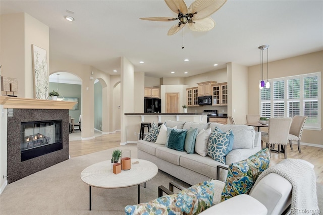 living room featuring a multi sided fireplace, ceiling fan, and light wood-type flooring