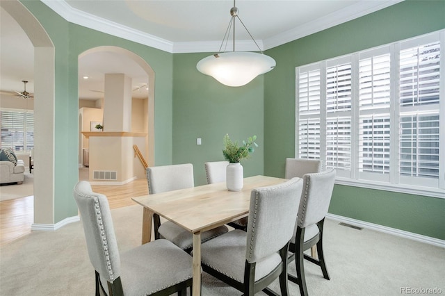 carpeted dining space with ceiling fan, crown molding, and plenty of natural light